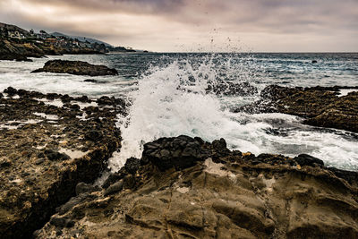 Waves splashing on rocks at shore against sky