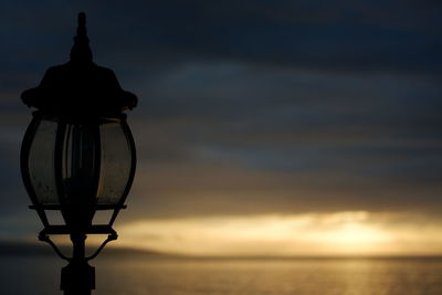 Street light by sea against sky during sunset