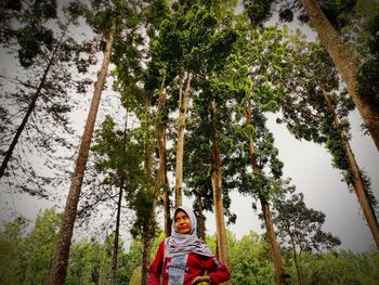 Woman in headscarf standing by trees in forest