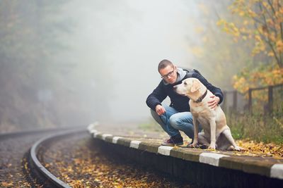 Young man with dog crouching by railroad track