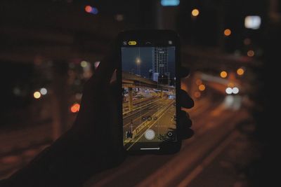 Man photographing illuminated smart phone at night