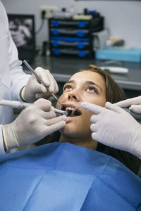 Dentist in surgical gloves doing dental treatment of female patient with help of assistant at clinic