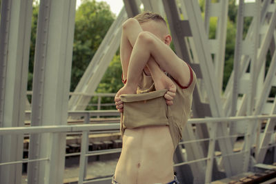 Man removing t-shirt while standing on bridge