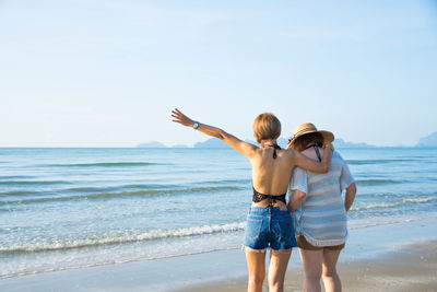 Rear view of female friends standing on shore at beach against sky