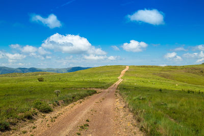 Scenic view of road amidst field against sky