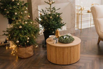 Several stylish christmas trees stand in the living room by the marble fireplace
