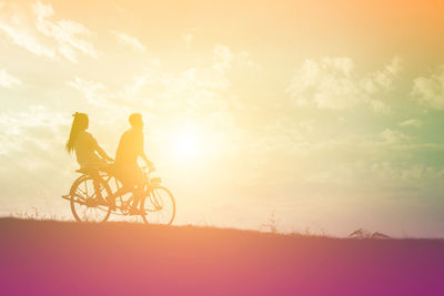 People riding bicycle on field against sky during sunset