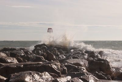 Waves splashing on rocks against sky