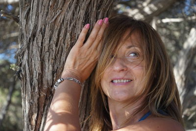 Close-up of woman looking away while touching tree trunk