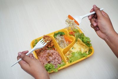 Cropped hands of person holding food in fork on table