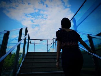 Rear view of woman standing on staircase against sky