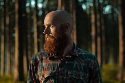 Thoughtful man with beard looking away against trees