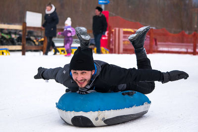 Playful man lying on sled at snow field