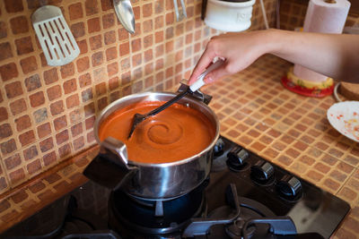 High angle of crop faceless female cook stirring hot marinara sauce prepared from tomatoes in saucepan on stove