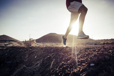 Low section of man running on land against sky during sunset