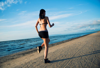 Rear view of young woman standing at beach against sky