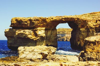 Rock formation by sea against clear sky