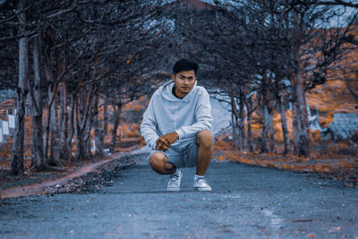 Full length portrait of young man sitting on road in forest