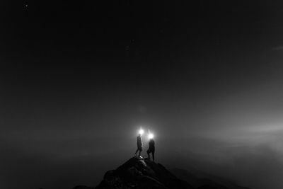 Silhouette people holding light on top of mountain against sky at night