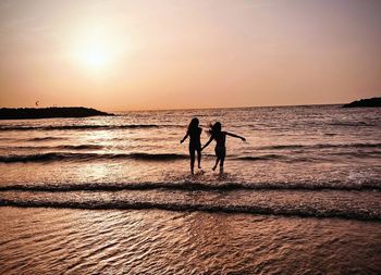 Silhouette woman walking at beach against sky during sunset