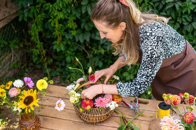 Cute florist girl collects a bouquet of autumn flowers in a basket on the table