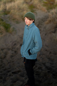 Teenage boy standing at the base of a dune on the coast at twilight