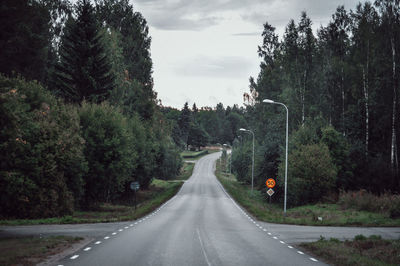 Empty road amidst trees against sky