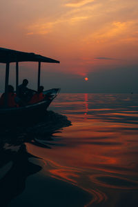 Silhouette men on boat in sea against sky during sunset