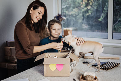 Happy family mom and kid putting bone in pet subscription box for dogs. chihuahua dog and