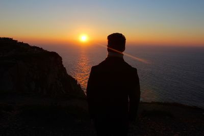 Silhouette man standing on rock against sea during sunset