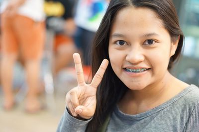 Close-up portrait of young woman showing peace sign