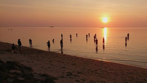 Silhouette people on beach against sky during sunset