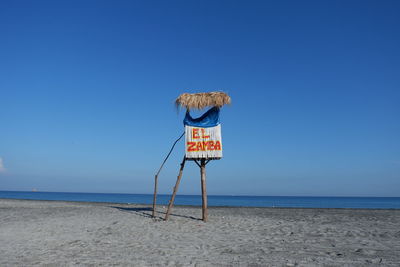 Lifeguard hut on beach against clear blue sky