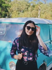 Young woman wearing sunglasses standing against car