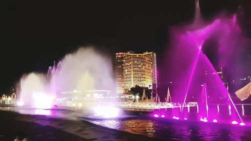 Illuminated buildings by river against sky at night