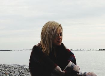 Young woman sitting on riverbank against sky