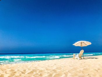 Chair on beach against clear blue sky