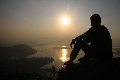 Silhouette man sitting on rock against sky during sunset