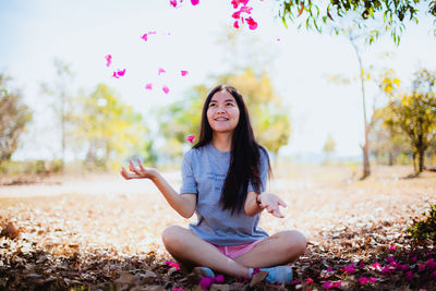 Young woman throwing flower petals while sitting on land