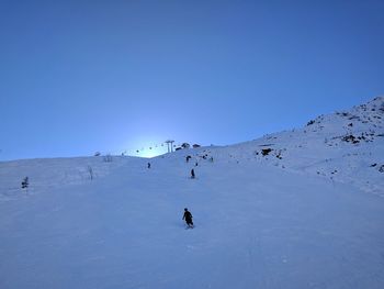 People on snow covered mountain against clear blue sky