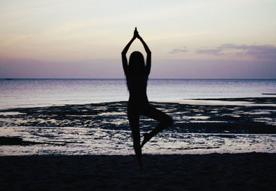 Silhouette woman exercising at beach against sky during sunset