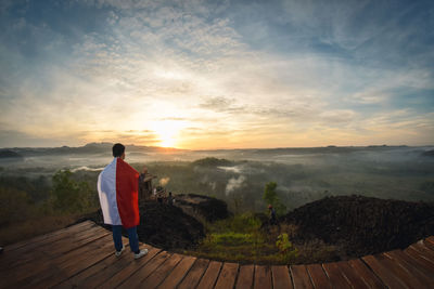 Rear view of man standing on mountain against sky during sunset