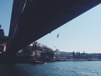 Low angle view of silhouette man jumping from bridge over river