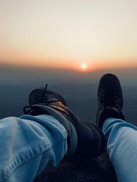 Low section of man standing on beach against sky during sunset