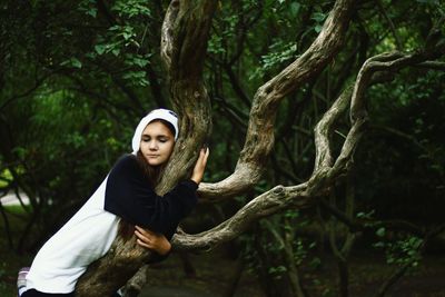 Young woman wearing panda costume embracing tree at forest