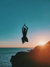 Silhouette boy jumping at sea against sky during sunset