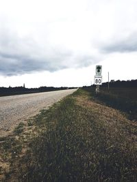 Road sign on field against sky