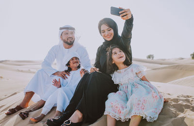 Young woman photographing family with phone at desert