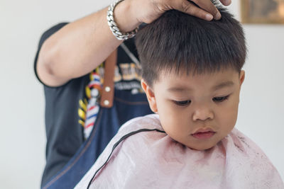 Midsection of barber cutting boy hair in salon