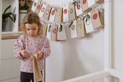 Toddler child gets new advent calendar task, waiting for christmas. festive mood for cute curly girl